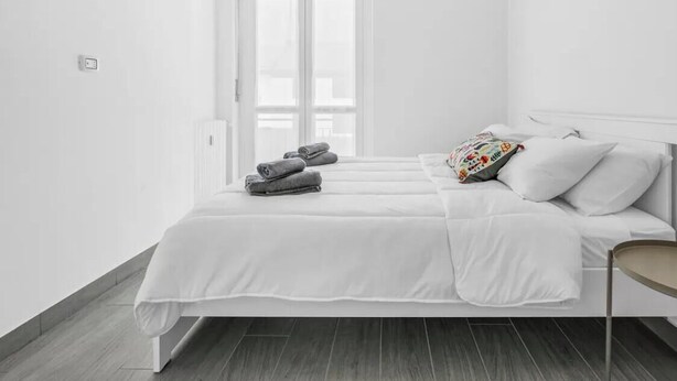 Een minimalistische slaapkamer met een bed, kussens en een raam.