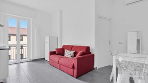 Een moderne woonkamer met een rode bank, een glazen eettafel en uitzicht door een schuifpui.
