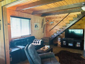 A cozy living room with a leather sofa, a television, a bookshelf, and a wooden staircase. - Family Friendly, Cozy 3-bedroom cabin in amazing Cascade with AC and Wood stove. (Cascade)
