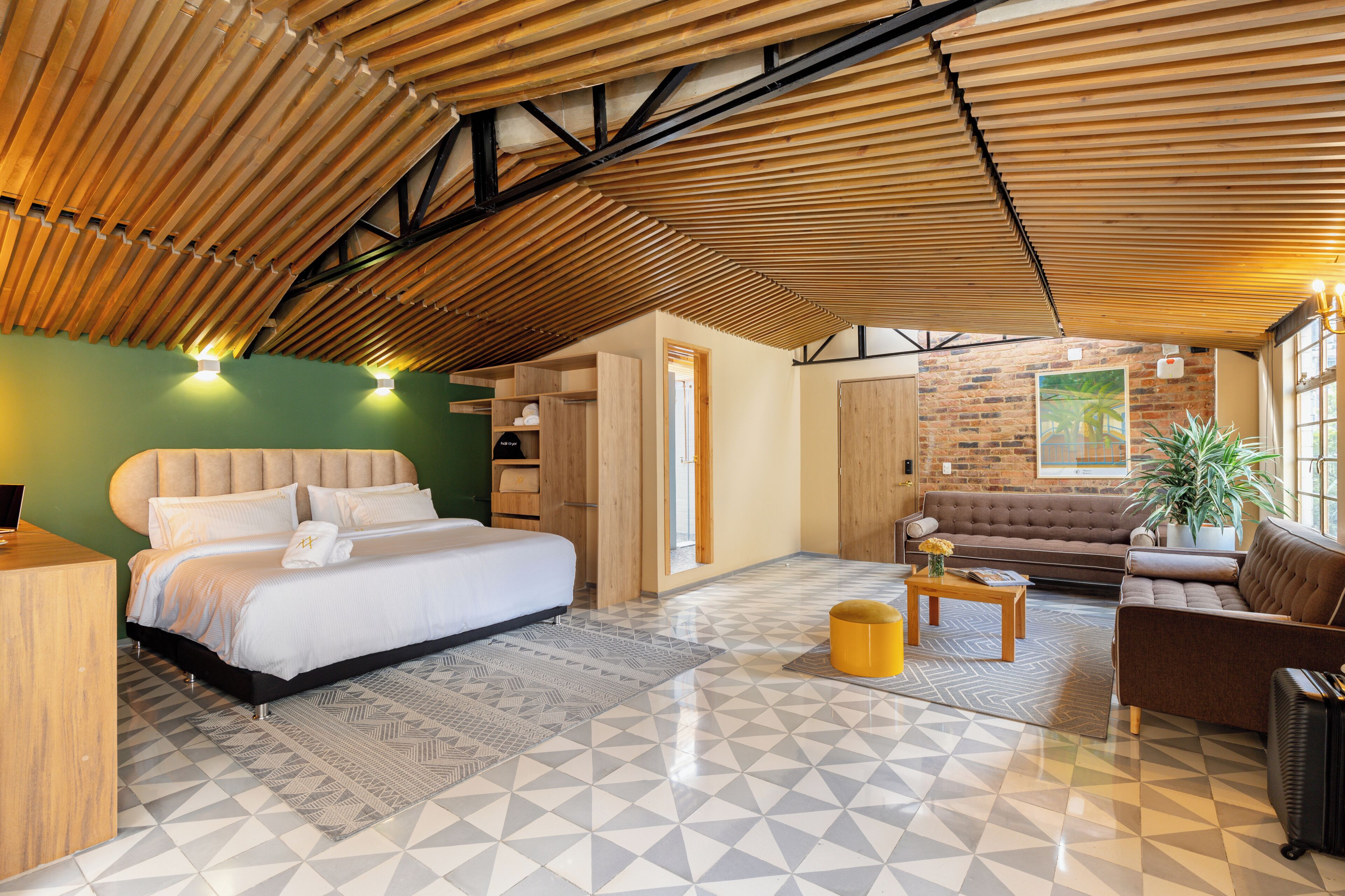 A modern hotel room with a bed, sofa, and a dining area.