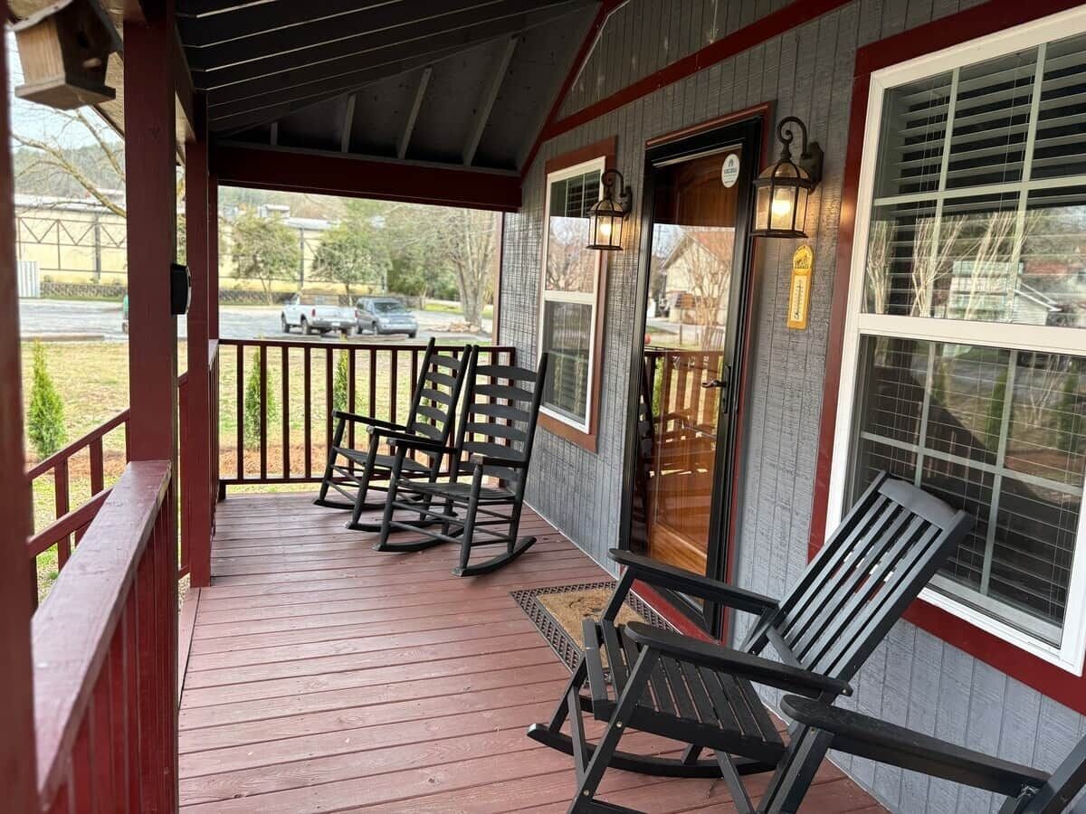 Une véranda couverte avec des fauteuils à bascule, une terrasse en bois et une vue sur la rue.