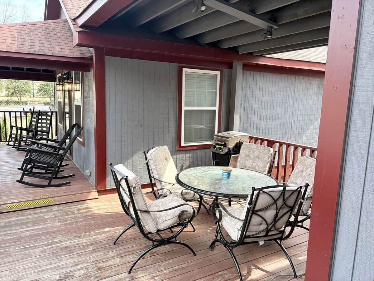 A covered patio with a round table and six chairs, a rocking chair, and a window.