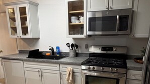 A kitchen with white cabinets, a microwave, stove, and a sink.