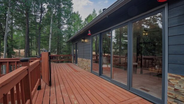 Une terrasse en bois avec des portes vitrées donnant sur un espace de détente extérieur, entouré d’arbres.