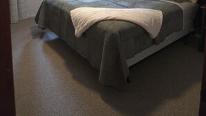Une chambre à coucher comprenant un lit, un ventilateur de plafond, une fenêtre avec des rideaux, une table de chevet avec une lampe et un miroir fixé au mur.