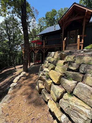 A cabin with a wooden deck and a stone retaining wall.