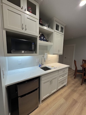 A kitchen with white cabinetry, a built-in microwave, a stainless steel dishwasher, and a wooden dining chair.