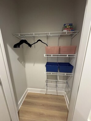 A closet with shelves and hanging space, containing storage bins and a box.