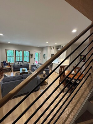 A modern living room with a staircase, wooden flooring, and a dining area with a table and chairs.