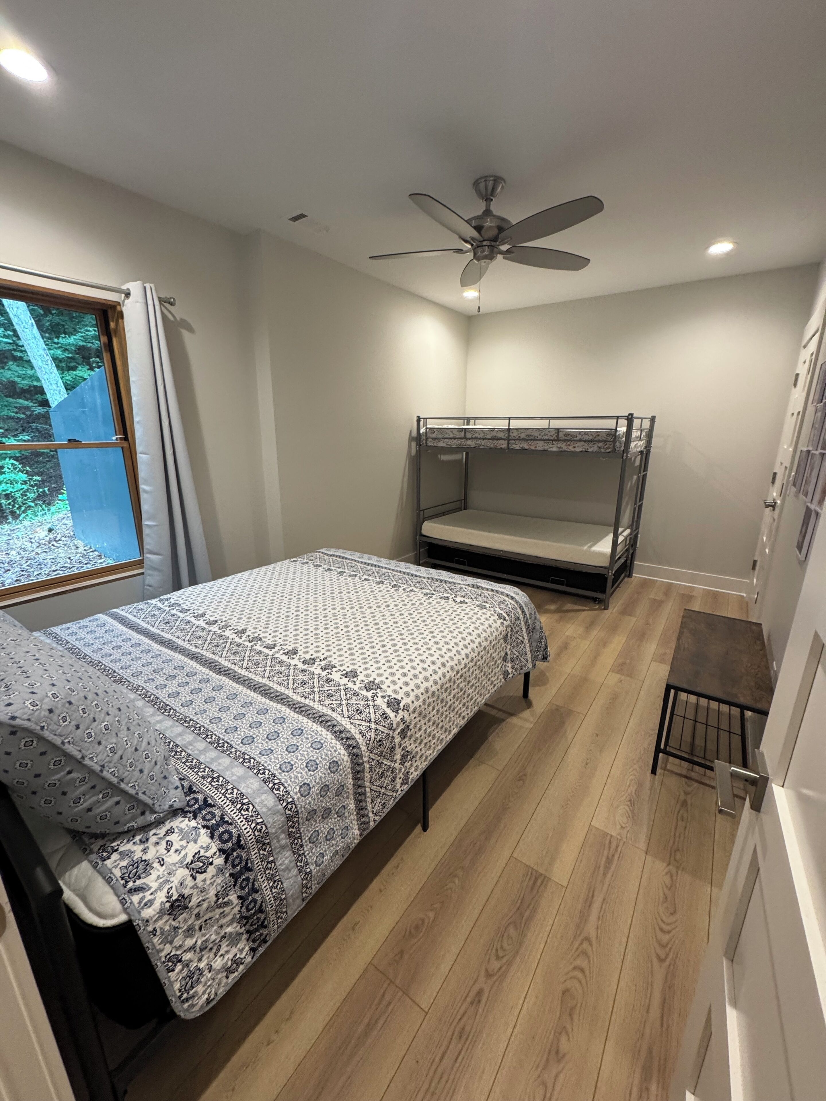 Ein kleines Schlafzimmer mit Etagenbett, einem Einzelbett mit gemusterten Textilien, einem Deckenventilator und einem Fenster mit Vorhängen.