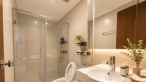 Een moderne badkamer met een douchecabine van glas, een wit toilet, een wastafelmeubel met een grote wastafel en een spiegel boven de spiegelkast.