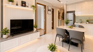 Een moderne keuken met een inbouwoven, een eethoek met een ronde tafel en stoelen, en een televisie bevestigd aan een wit kastje.