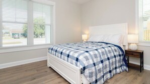 Una camera da letto con un letto, due lampade sui comodini, una ventola a soffitto e ampie finestre con tende.