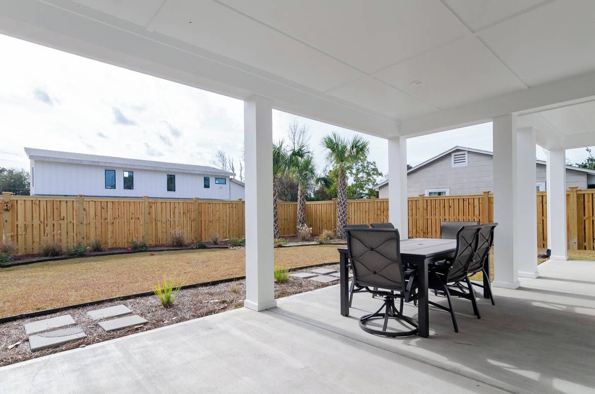 A covered patio area with a table and chairs, a wooden fence, and a building in the background.