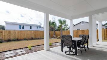 A covered patio area with a table and chairs, a wooden fence, and a building in the background.