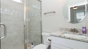 Un bagno moderno con box doccia in vetro, un water, un lavabo con piano in marmo e uno specchio.