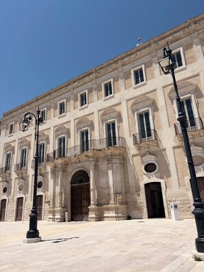 Un bâtiment historique doté de nombreuses fenêtres, d’une entrée centrale surmontée d’une arche et d’une cour pavée.