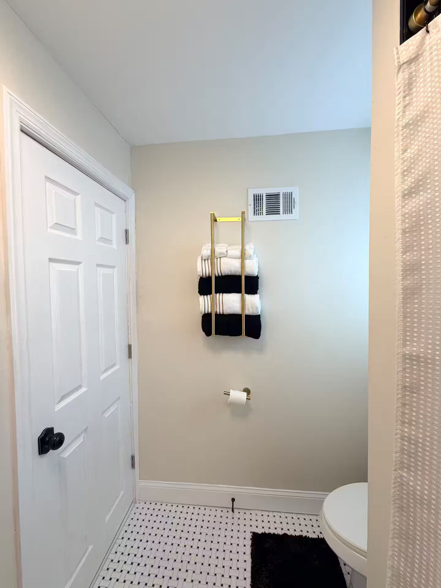 A bathroom with a white door, a towel rack with folded towels, a toilet, and a patterned floor.