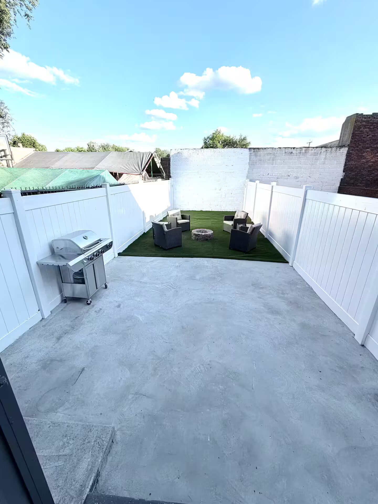 Un patio con una parrilla, mobiliario exterior y una cerca blanca.