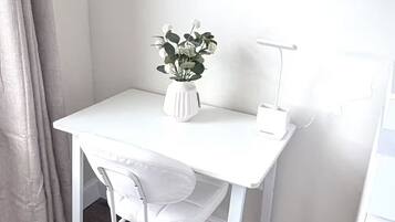 A white desk with a chair, a white vase with flowers, and a desk lamp.