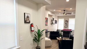 Uma sala de estar moderna com lareira, uma sala de jantar com mesa de bilhar e um corredor com extintor de incêndio.