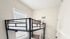 Uma cama beliche com cabeceira, uma janela com persianas, uma porta e um tapete estampado.