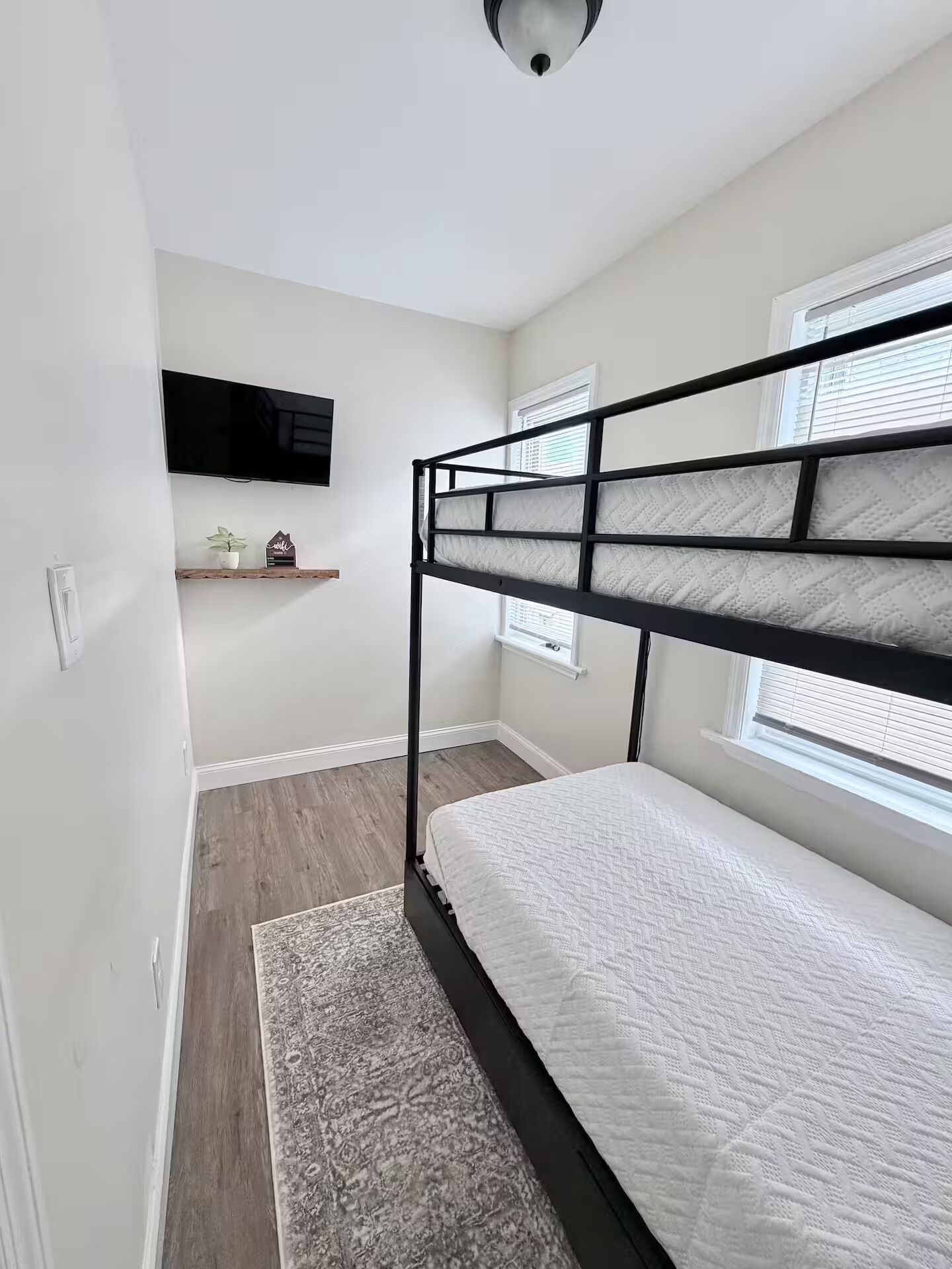 A compact bedroom with a bunk bed, a flat-screen TV mounted on the wall, and a small shelf with decorative items.