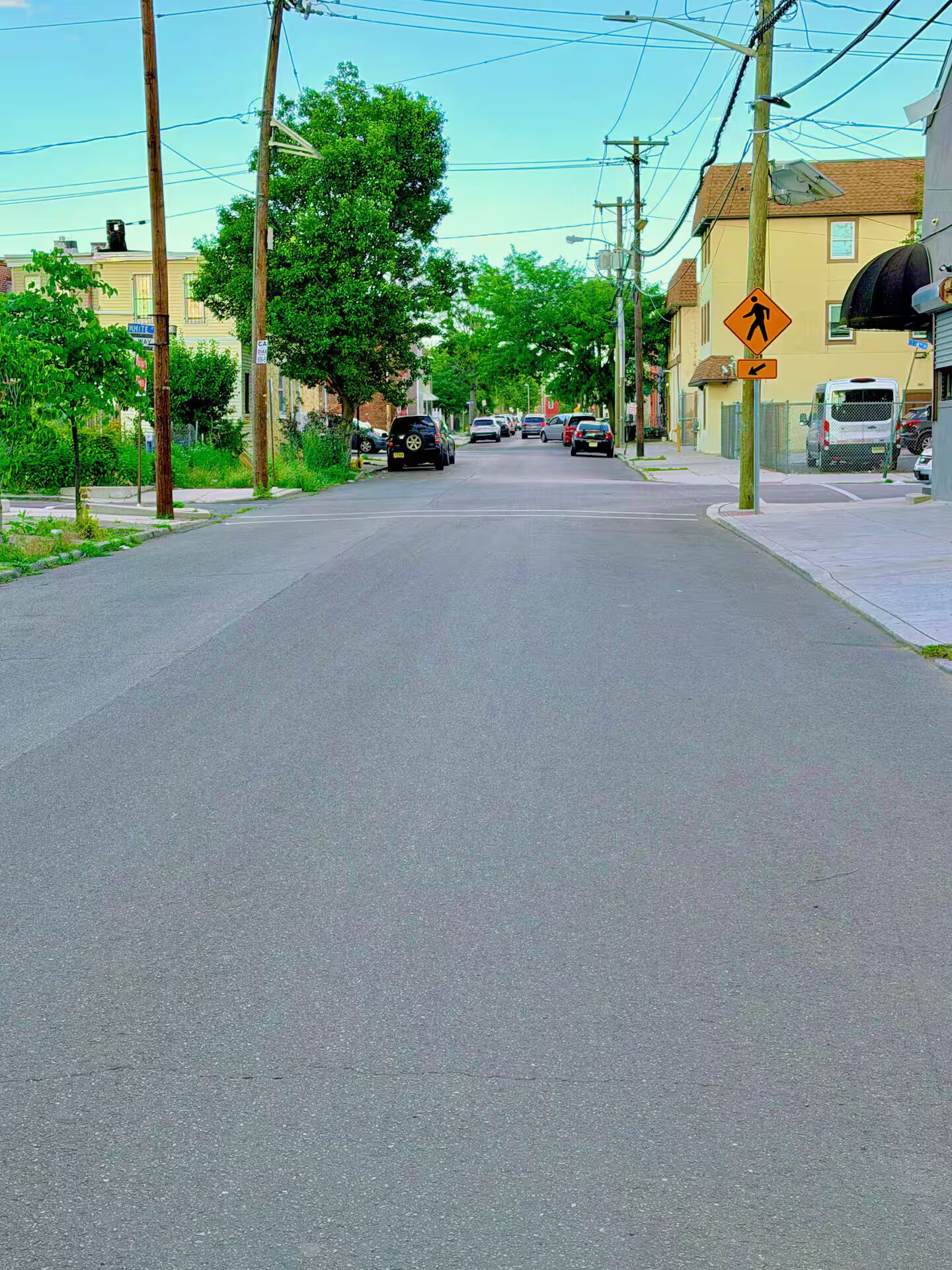 A residential street with houses, parked cars, and a pedestrian crossing sign.