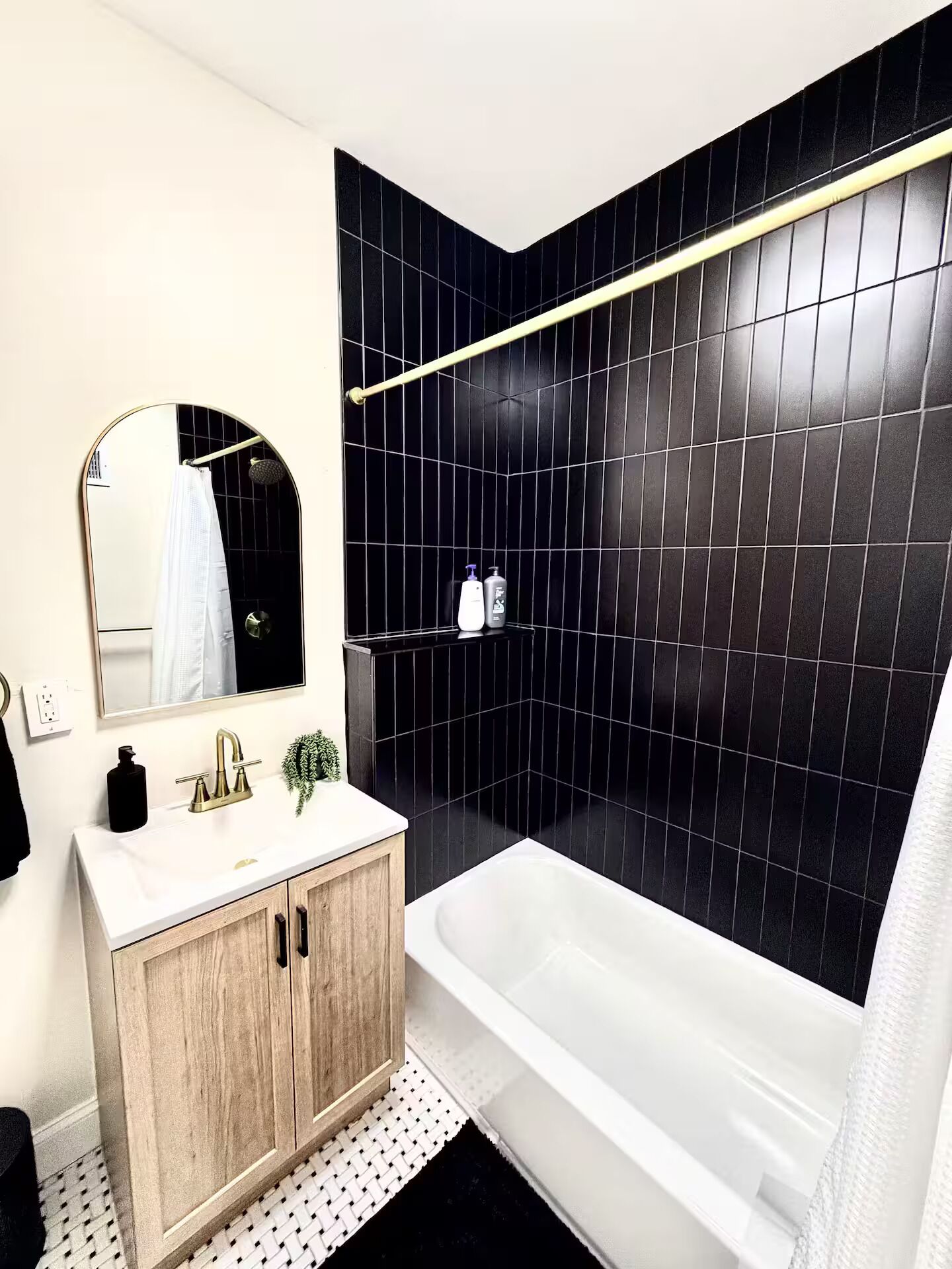 Un baño moderno con bañera, tocador con espejo y zona de ducha con azulejos negros.