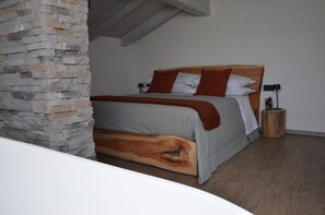 A bedroom with a stone pillar, a wooden headboard, a bed with grey bedding, and a nightstand with a lamp. - Mountain Suite apartment with a sauna and an open-plan bathtub (Sanzeno)
