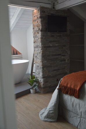 A modern bathroom with a stone accent wall, a bathtub, and a potted plant. - Mountain Suite apartment with a sauna and an open-plan bathtub (Sanzeno)