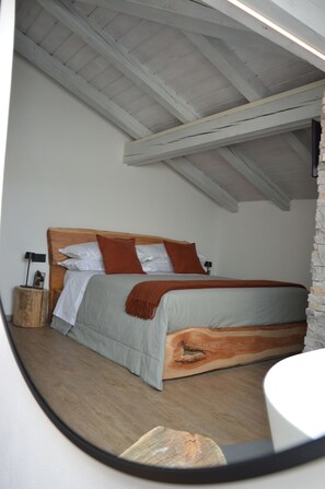A bedroom with a wooden headboard, a bed with white and brown bedding, a nightstand with a lamp, and a stone wall. - Mountain Suite apartment with a sauna and an open-plan bathtub (Sanzeno)