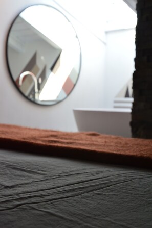 A round mirror reflecting a bathroom interior, a wooden ledge, and a wall with a white sink. - Mountain Suite apartment with a sauna and an open-plan bathtub (Sanzeno)
