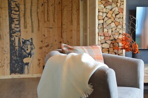 A room with a grey sofa, a blanket, and a patterned pillow. A wall with a wooden texture and a painting of a wolf is visible. - Mountain Suite apartment with a sauna and an open-plan bathtub (Sanzeno)