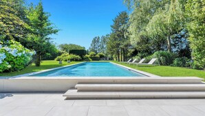 Ein rechteckiger Pool mit Stufen, umgeben von einer gepflegten Rasenfläche und verschiedenen Bäumen.