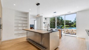 A modern kitchen with a central island, built-in shelves, and a view of an outdoor pool area.