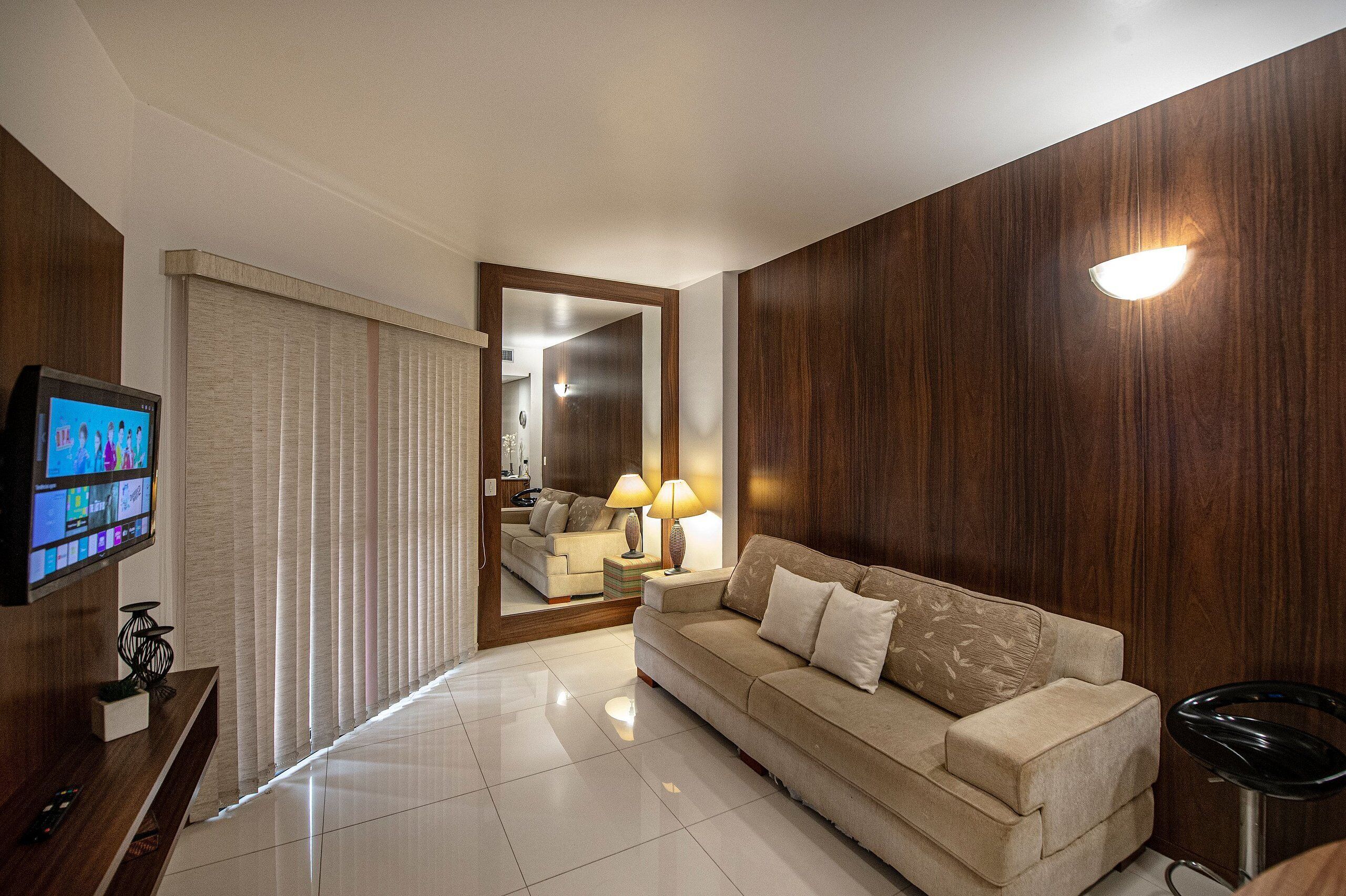 Uma sala de estar moderna com um sofá bege, uma televisão e uma parede de destaque em madeira.