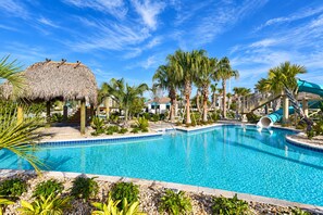 Una piscina con tobogán, palmeras y una estructura con techo de paja.