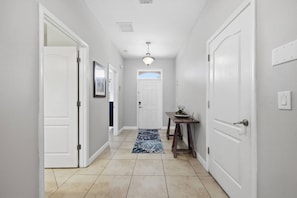 A hallway with white doors, a tiled floor, and a ceiling light fixture. - 9BR Resort Home for Large Groups with Private Pool Near Disney (Four Corners)