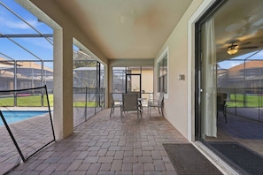 Un patio cubierto con piscina, mobiliario exterior y vista a un barrio residencial.