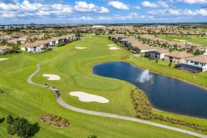 A golf course with bunkers, a pond, and residential buildings. - 9BR Resort Home for Large Groups with Private Pool Near Disney (Four Corners)