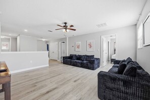 A spacious living area with a ceiling fan, hardwood flooring, and a dark-colored sofa. - 9BR Resort Home for Large Groups with Private Pool Near Disney (Four Corners)