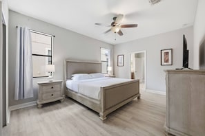 Un dormitorio con cama, mesitas de noche, ventilador de techo y cómoda.