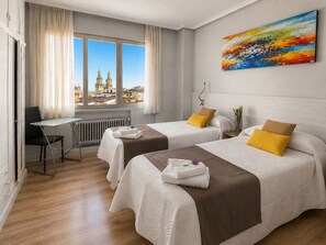 Habitación de hotel con dos camas, un escritorio y vistas a la ciudad.