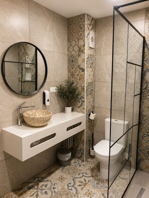 A bathroom with a round mirror, a vessel sink, a toilet, and a shower enclosure.