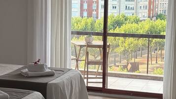 Une chambre d’hôtel avec deux lits, un balcon doté d’une table et de chaises, et une vue sur des immeubles et des arbres.