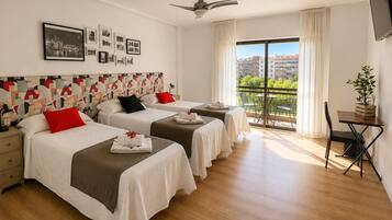 Una habitación de hotel con dos camas, ventilador de techo, balcón con vistas y televisor montado en la pared.