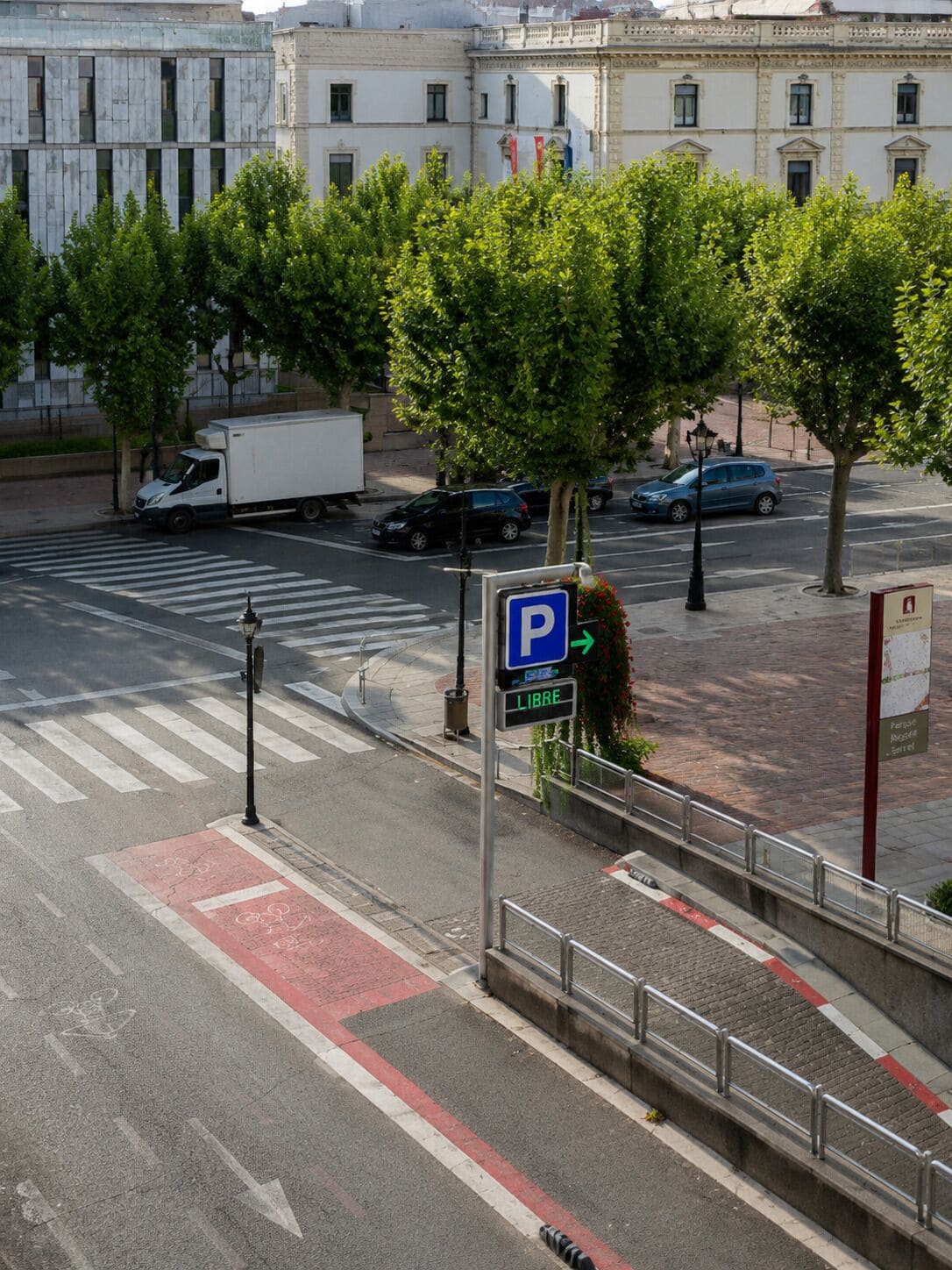 Vista de una calle con señal de estacionamiento, paso de peatones y un edificio de arquitectura clásica.