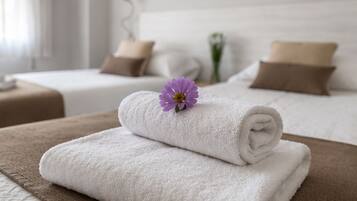 A hotel room with two beds, each with a brown pillow and a white headboard. A rolled white towel is placed on a brown towel on the bed.