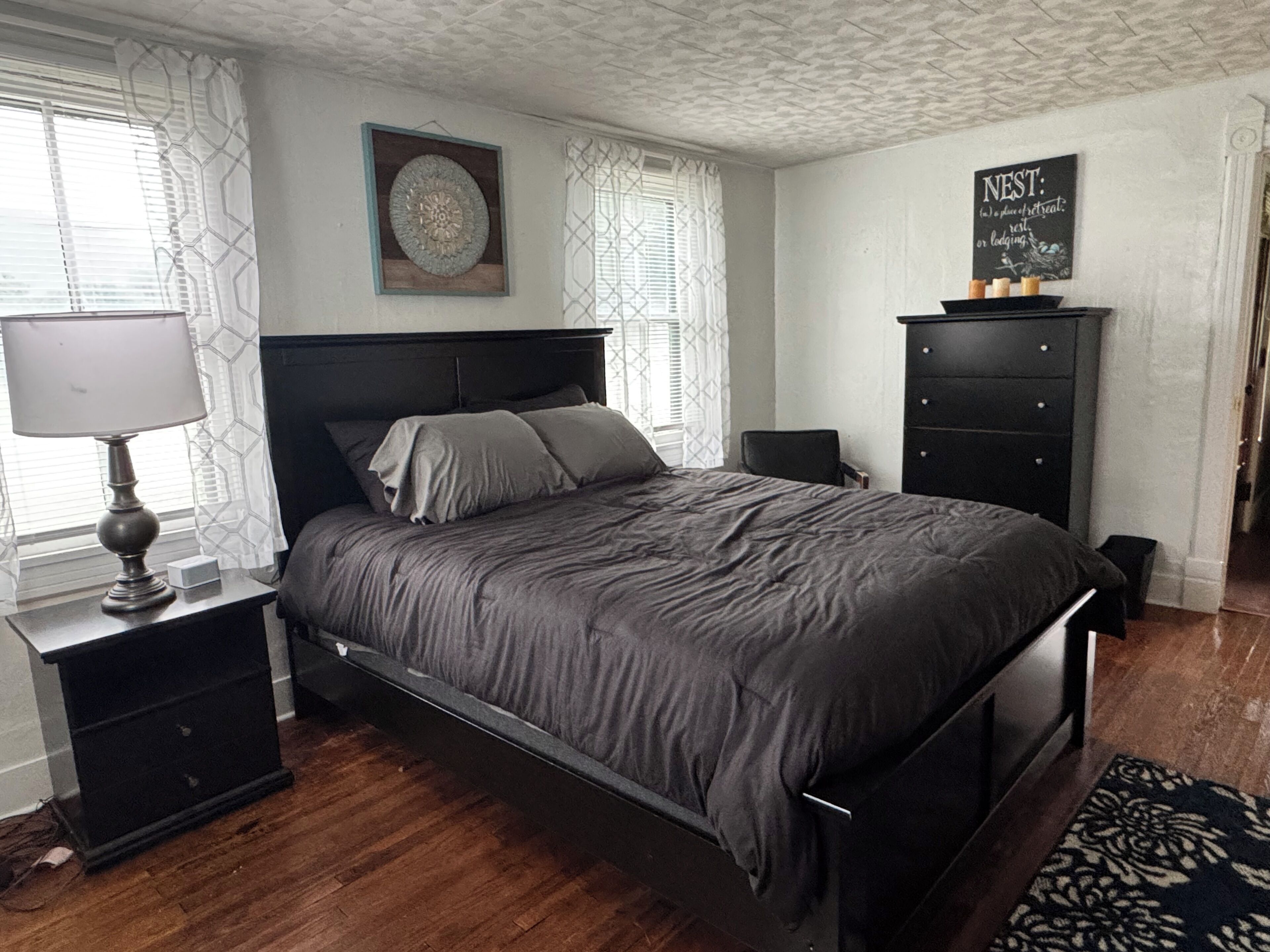 Un dormitorio con cama, mesitas de noche, cómoda y una lámpara de pared.